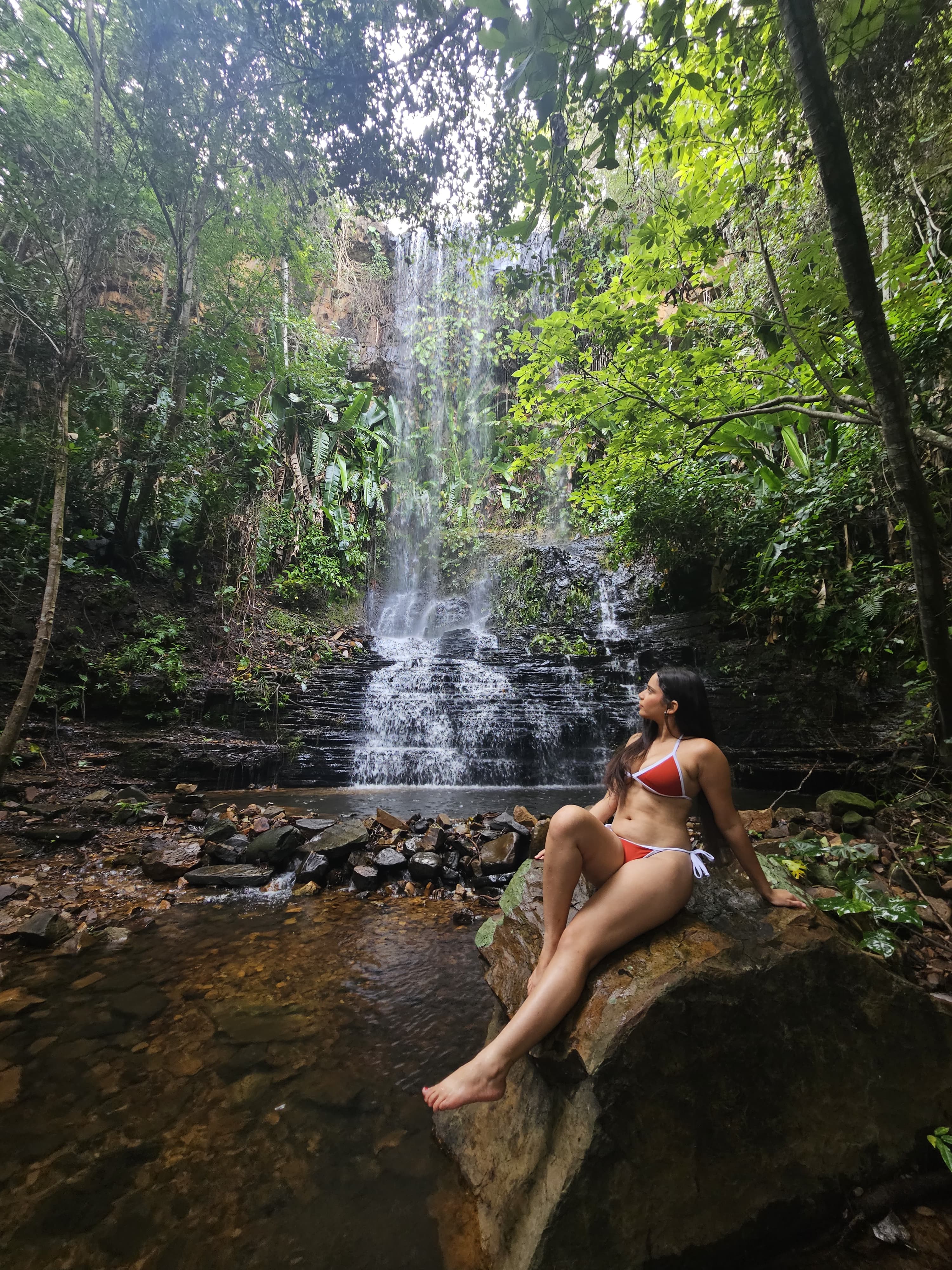 sentada sobre pedra à frente de uma cachoeira
